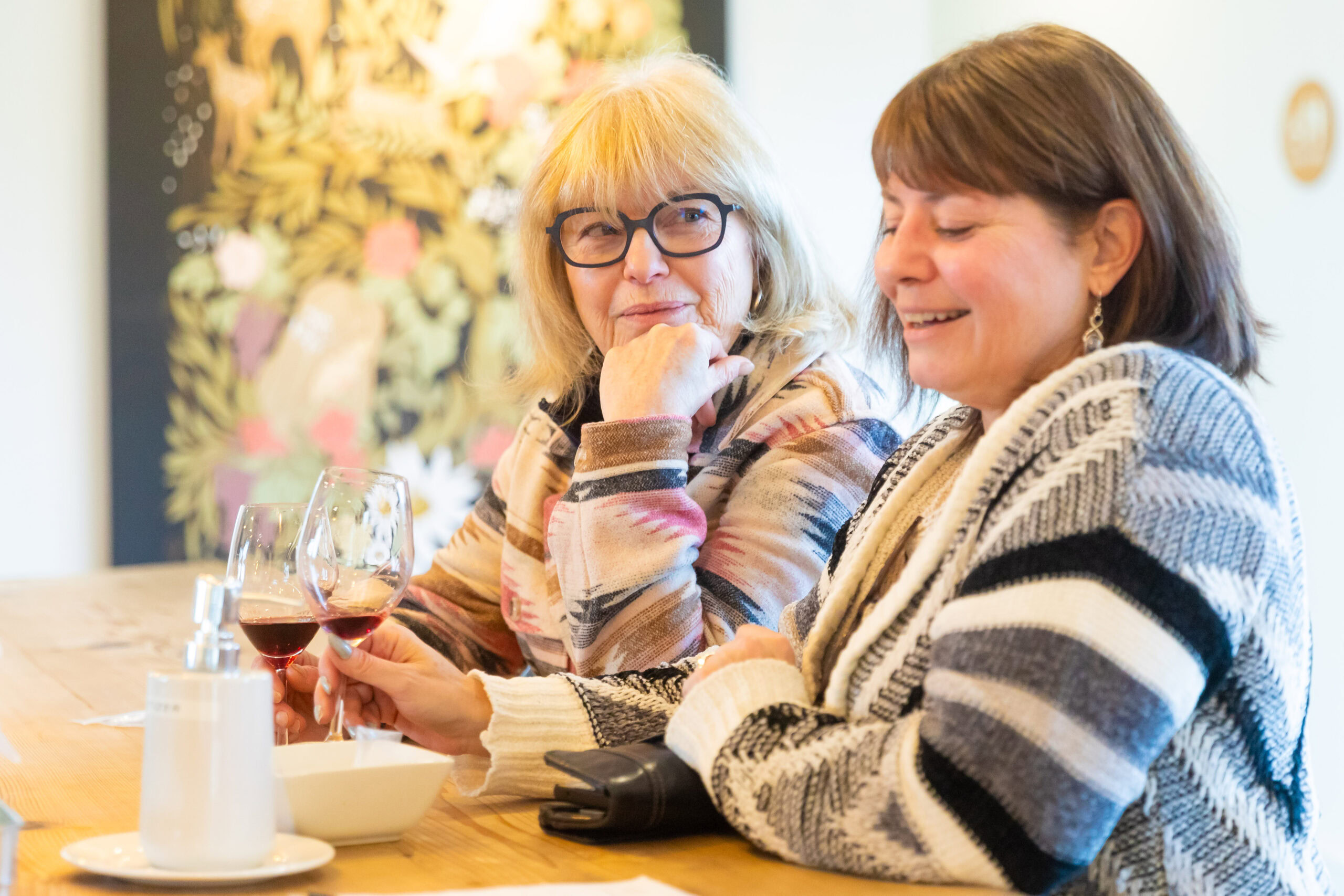 Two women enjoying wine at a winery social event, smiling and chatting.
